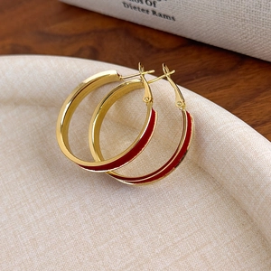 Detail of red velvet enamel hoop earrings with polished gold-plated finish on fabric tray