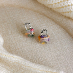 Détail des boucles d'oreilles en laine arc-en-ciel sur fond en tricot douillet