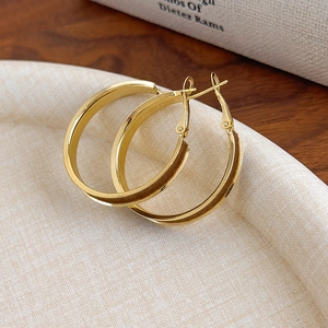 Detailed close-up of wide gold-plated hoop earrings on a textured jewelry tray