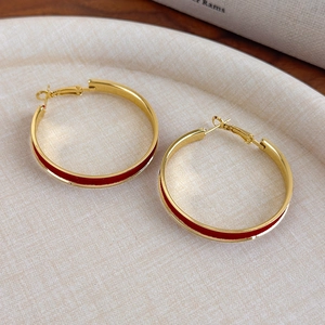 Detail of gold hoop earrings with red enamel inlay on a textured beige display