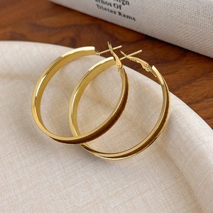 Detail of red velvet and gold metal hoop earrings on a textured cream jewelry tray