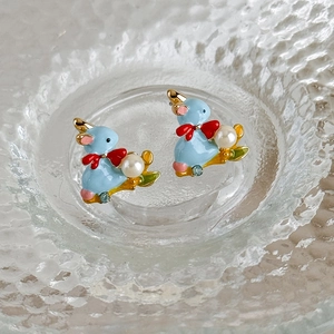 Cute blue enamel bunny stud earrings with pearl and bow detail in a glass dish