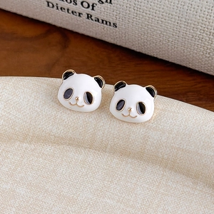 Dettaglio di orecchini a lobo panda in smalto dorato su un supporto in legno minimalista