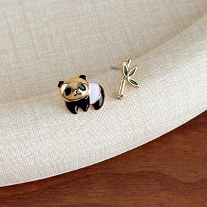 Vista macro di orecchini asimmetrici a forma di panda e bambù smaltati su tessuto bianco