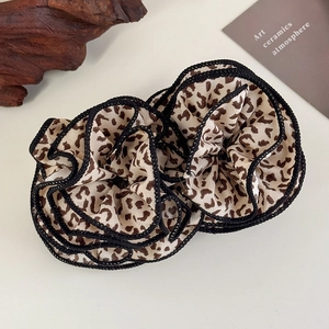Detail showing two leopard print scrunchies with black edges on a minimalist background