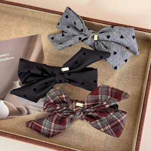 Three elegant fabric bow hair clips with heart, polka dot and plaid patterns on tray