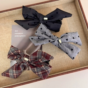 Three bow hair clips with heart and plaid patterns on a woven tray with gold metal tags