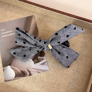 Detail of grey fabric bow hair clip with black heart patterns and a gold metal tag