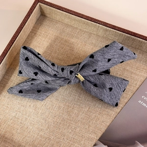 Detail of grey bow hair clip with black heart patterns and golden metal tag