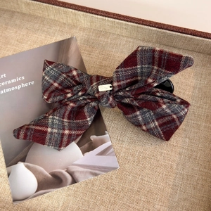 Detail of British style plaid bow hair clip with a gold metal tag on a textured tray