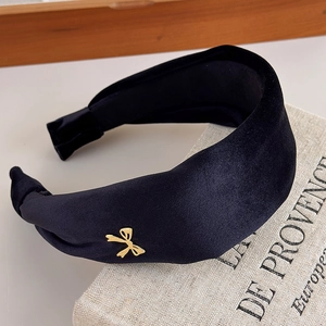 Detail of a vintage black velvet wide headband with a small gold metal bow accent