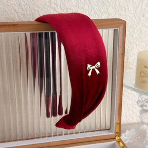 Detail of burgundy velvet wide headband featuring a gold metal bow on textured glass