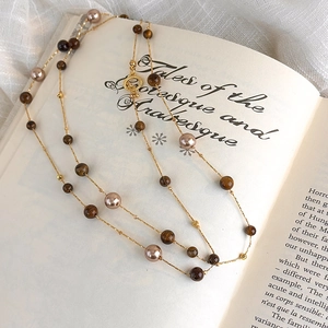 Detail of tiger eye beads and pearls on gold chain draped over an antique book