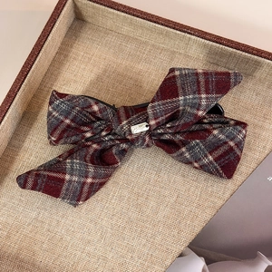 Detailed view of red and grey plaid bow hair clip with silver metal tag on linen tray