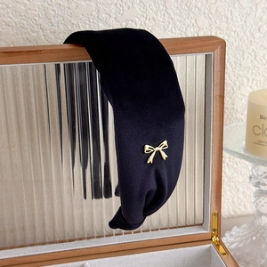 Detail of a black velvet wide headband with a gold metal bow accessory on a jewelry box