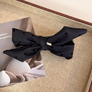 Detail of black polka dot bow hair clip featuring a square gold metal logo accent
