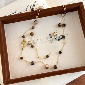 Detail of tiger eye and pearl long necklace inside a vintage jewelry box with books