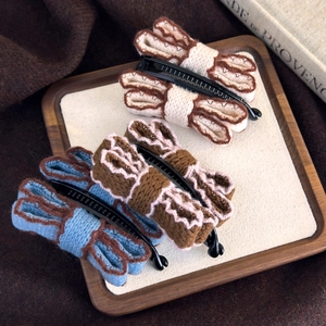 Three vintage knitted bow banana hair clips in cream, brown and blue on a tray