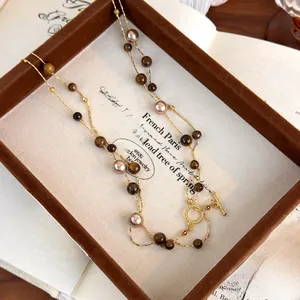 Detailed close-up of tiger eye stone and purple pearl necklace with golden OT buckle