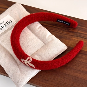 Detailed view of red plush headband with beige bow embroidery and handmade woven label