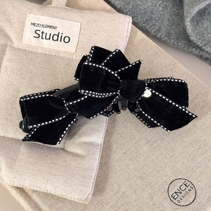 Elegant black velvet bow hair clip with white stitching on a minimalist fabric background