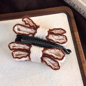 Detail of knitted bow banana hair clip with cream fabric and brown stitching texture
