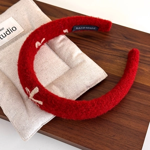 Close-up of red plush crochet headband with cross embroidery and handmade label detail