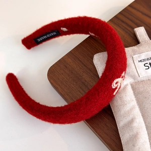 Detail of red plush headband with white embroidered bow and HAND MADE woven label