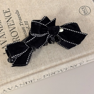 Close-up of a luxury black velvet bow hair clip with white stitching on a book