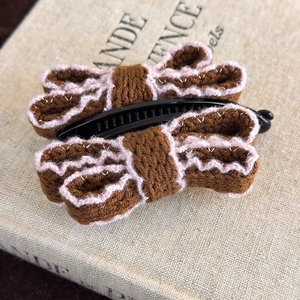 Detail of a brown knitted bow hair clip with pink wave stitching on a vintage book