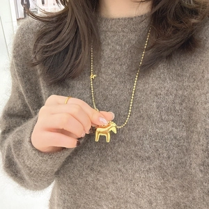Close-up of a golden horse pendant with bead chain on a dark grey knit sweater
