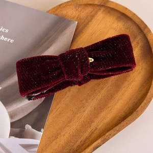 Close-up of burgundy velvet bow hair clip with silver glitter on wooden tray