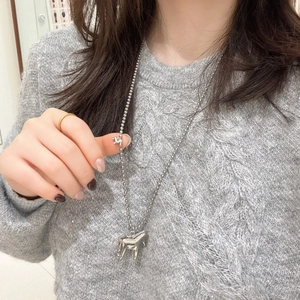 Detailed view of silver dual horse pendant on bead chain worn over gray knit sweater