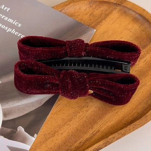 Close-up of burgundy velvet bow banana clip with silver glitter on wooden tray