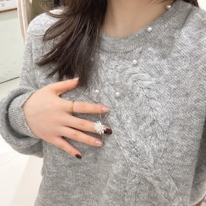 Détail d'un pull gris en maille torsadée avec perles et pendentif floral à pampilles