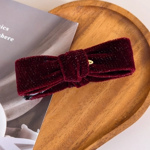 Detail view of burgundy velvet bow hair clip with fine glitter on a wooden tray