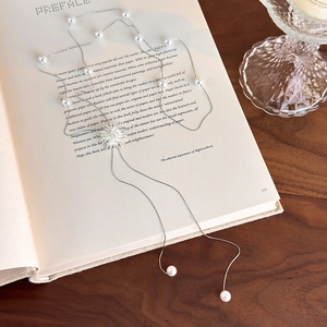 Collier élégant à pompon perlé et pendentif tournesol sur fond de livre ouvert