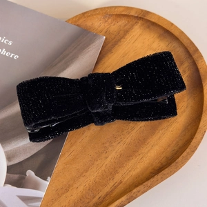 Close-up of black velvet bow hair clip with gold glitter on a wooden tray