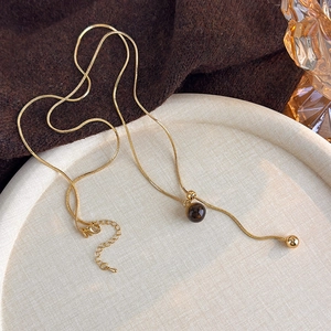 Detailed shot of golden Y-shaped tiger eye necklace on textured dish with autumn vibes