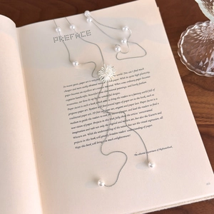 Sautoir argenté avec perles blanches sur livre ancien pour un look élégant et chic