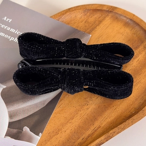 Close-up of black velvet bow banana hair clips with subtle shimmer on a wooden tray