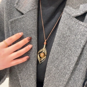 Gros plan d'un collier pendentif feuille dorée avec perle oeil de tigre sur pull noir