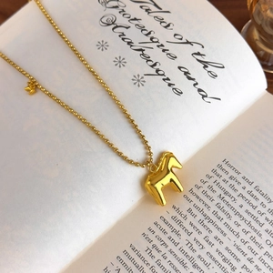 Macro detail of golden ball chain necklace with horse head pendant on vintage book