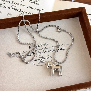 Close-up of a polished silver horse pendant on a ball chain necklace over a jewelry tray