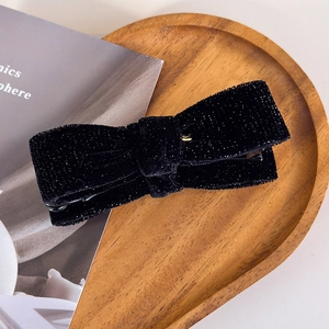 Close-up of vintage black velvet bow hair clip with fine glitter on a wooden tray