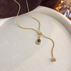 Macro detail of golden snake chain with teardrop tiger eye stone pendant on beige tray