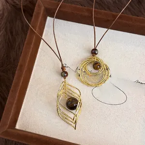 Gros plan de pendentifs feuilles dorées avec pierre œil de tigre sur un cordon marron