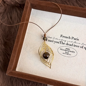 Gros plan du pendentif feuille dorée avec œil de tigre dans un coffret à bijoux