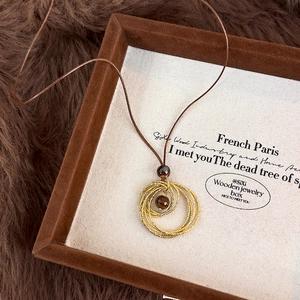 Vue détaillée du pendentif doré multi-anneaux avec perle oeil de tigre sur velours marron