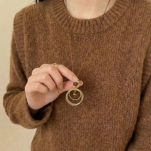 Collier long doré avec pierre oeil de tigre sur un pull en maille marron